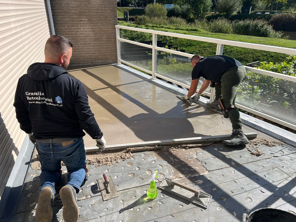Twee medewerkers van Grandia Betonherstel brengen een nieuwe afwerklaag aan op het balkon