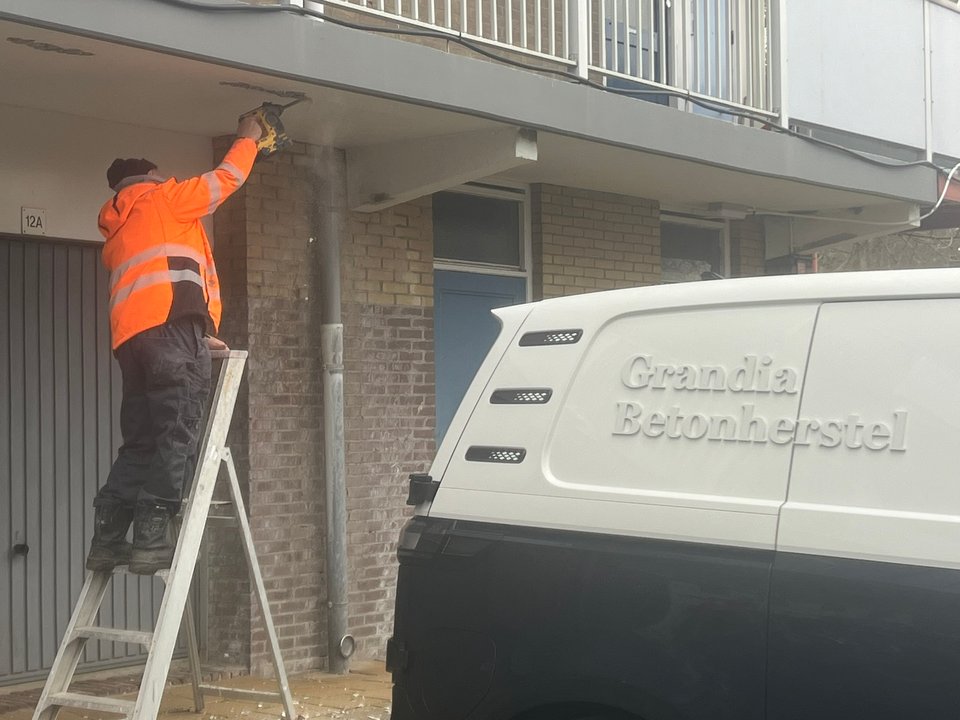 Bus van Grandia Betonherstel bij een galerijflat, medewerker aan het werk op een ladder